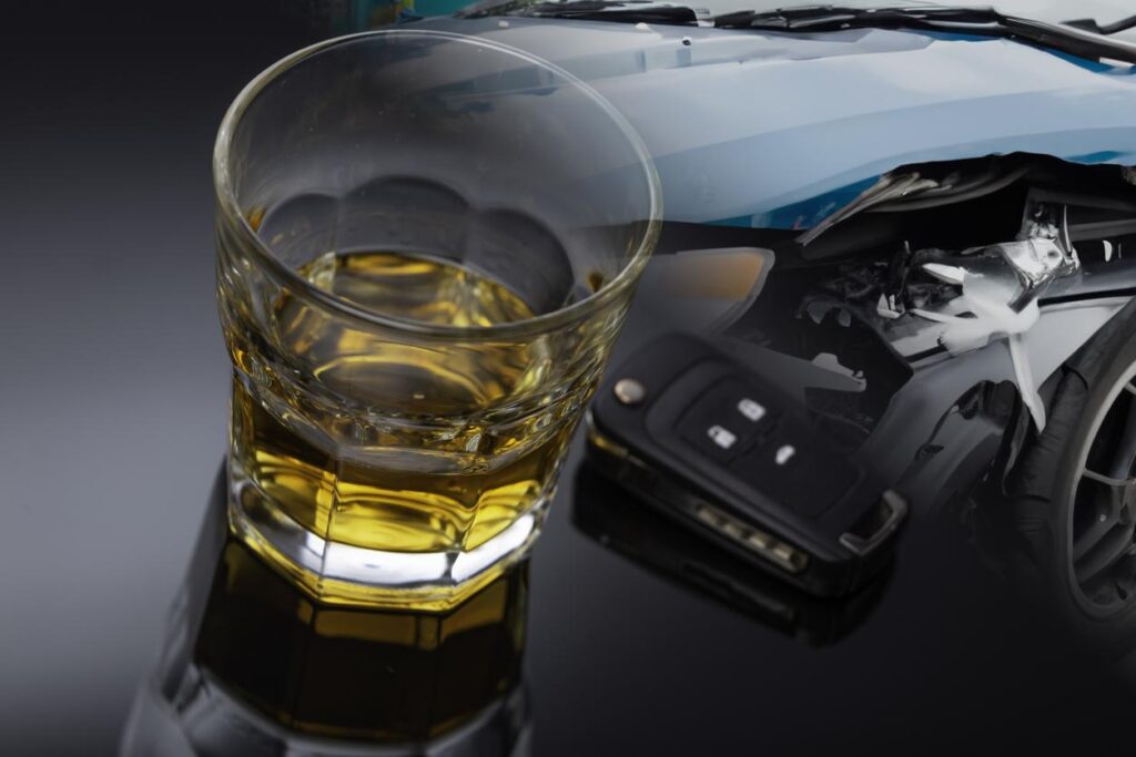 A glass of brown alcohol sitting beside an electronic car key with a background image of a car accident in the upper right corner.